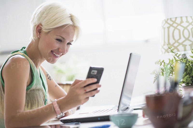 Woman using cell phone and laptop at home.