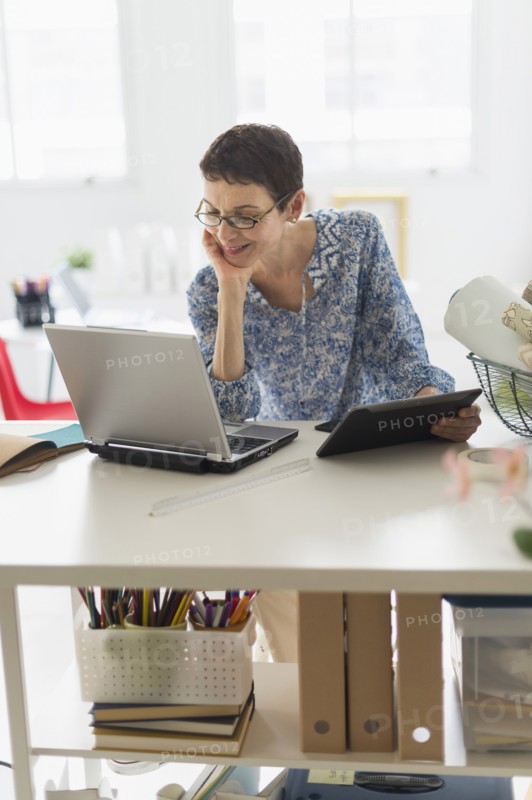 Senior business woman using cell phone and tablet pc in office.