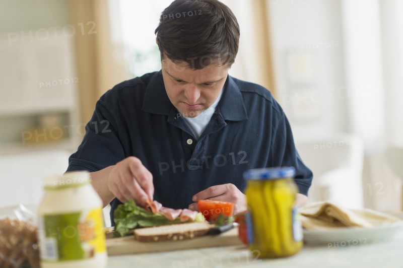 Man with down syndrome making sandwich.
