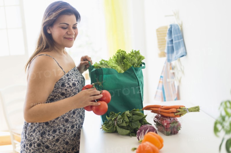 Woman taking out vegetables of grocery bag.