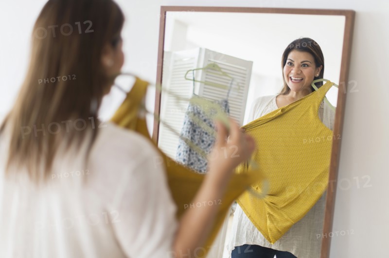 Woman holding new dress and looking at mirror.