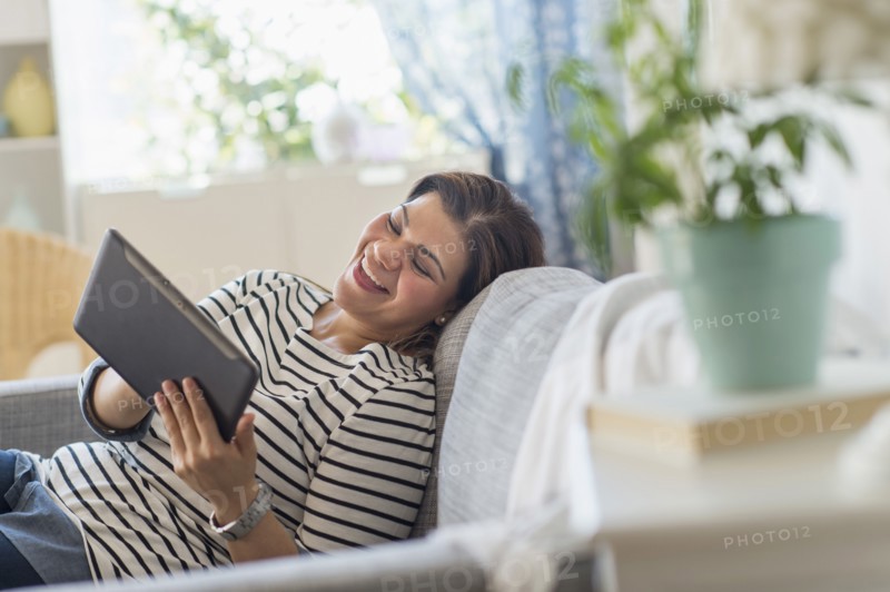 Portrait of happy woman lying on sofa with tablet pc.