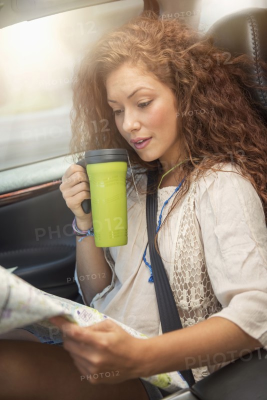 Woman sitting in car with map and disposable cup.