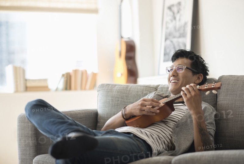Man sitting on sofa and playing ukulele.