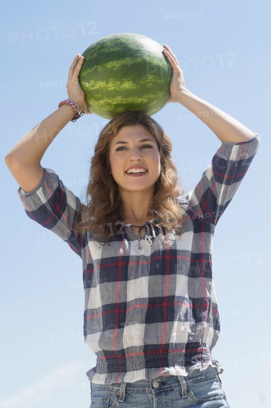 Young woman carrying on head watermelon.