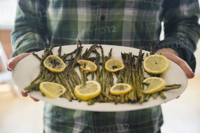 Man holding platter with asparagus and lemon