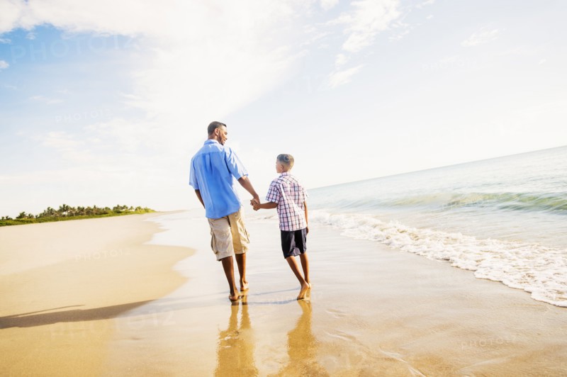 Father and son (10-11) walking on beach