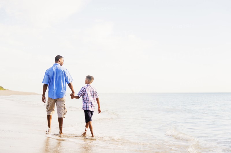 Father and son (10-11) walking on beach