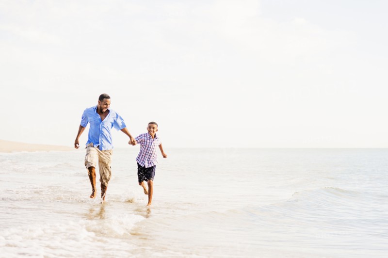 Father and son (10-11) running on beach
