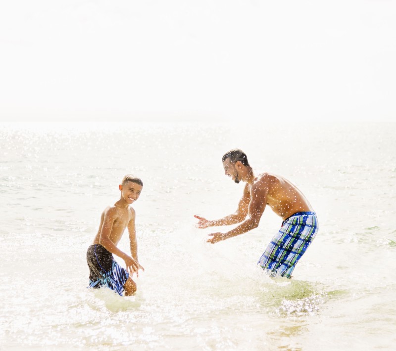 Father and son (10-11) having fun on beach