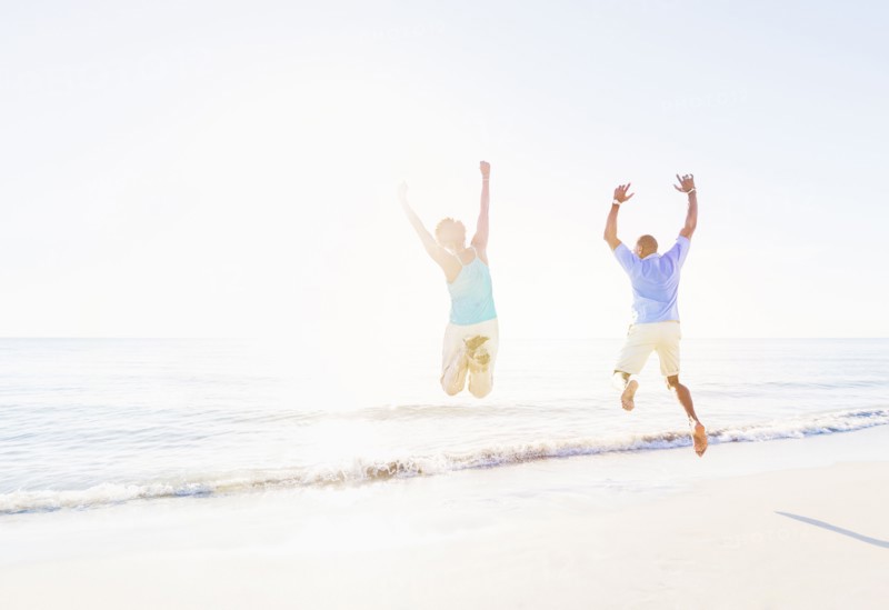 Mature couple jumping in sea with arms raised