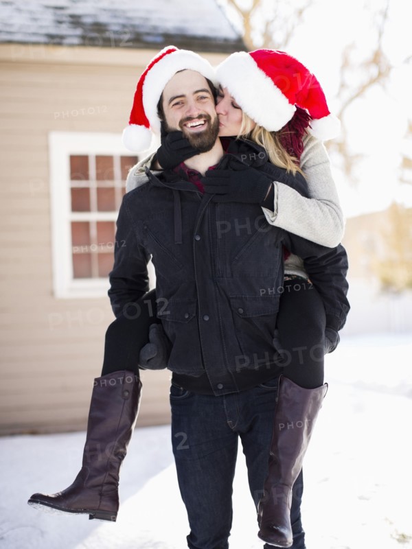 Portrait of young couple in santa hats, piggyback