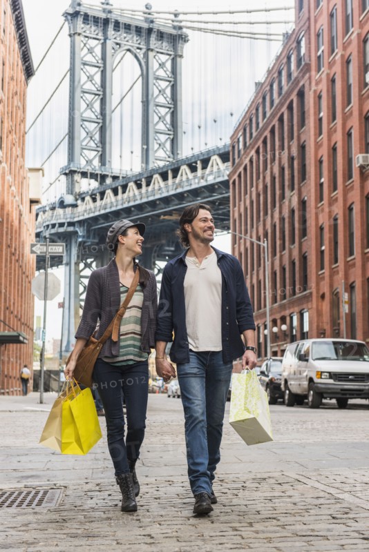 Couple walking on street, Brooklyn Bridge in background. Brooklyn, New York.