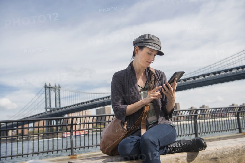 Woman using tablet pc, Manhattan Bridge in background. Brooklyn, New York.