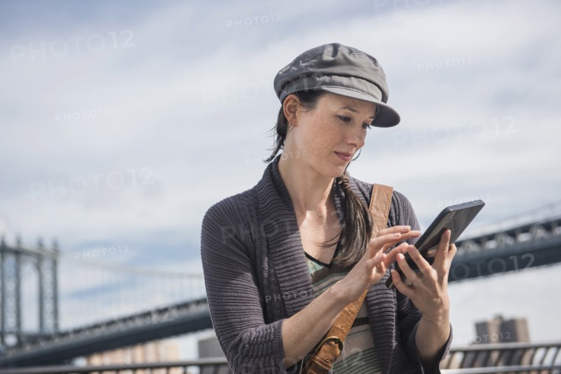 Woman using tablet pc, Manhattan Bridge in background. Brooklyn, New York.
