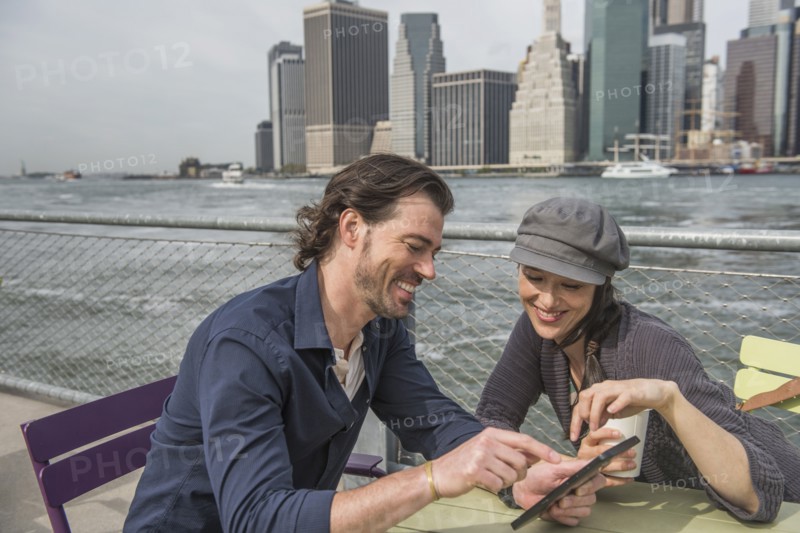 Happy couple sitting and using tablet pc with cityscape in background. Brooklyn, New York.