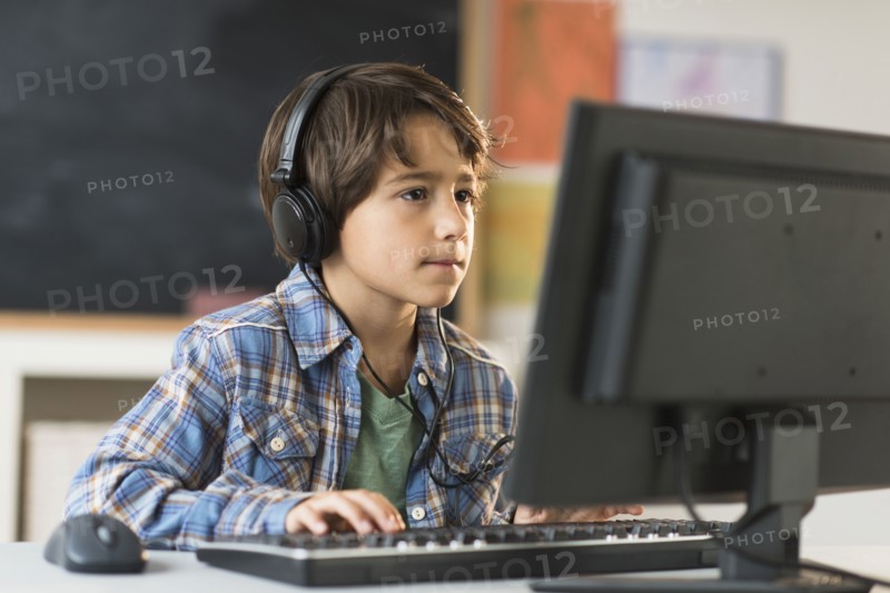 Schoolboy (6-7) using computer in classroom.