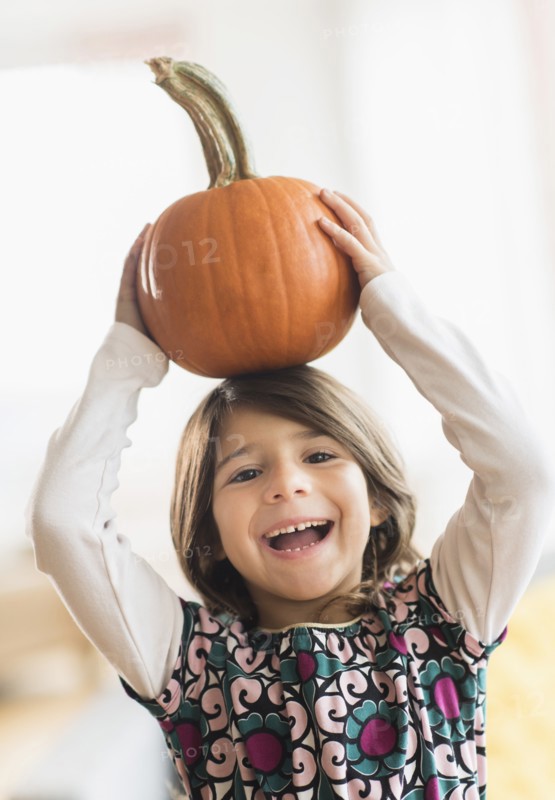 Portrait of happy girl (6-7) with pumpkin on head.