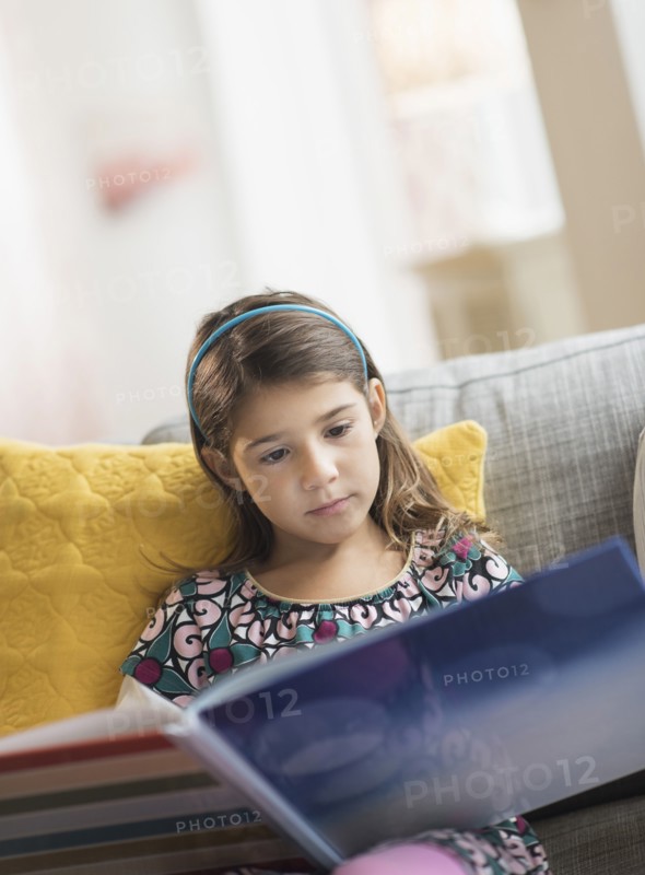 Girl (6-7) reading book at home.