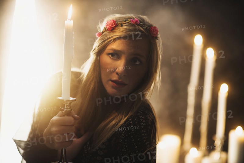 Sorceress holding candle in dark room.