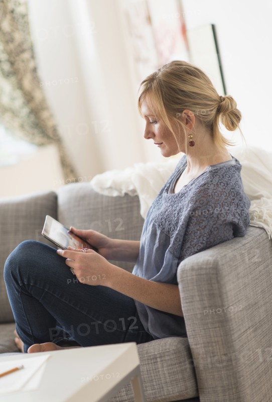 Pensive woman sitting on sofa with tablet pc.