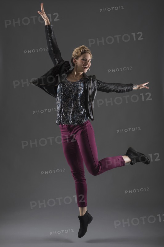 Studio shot of cheerful woman jumping with arms raised.