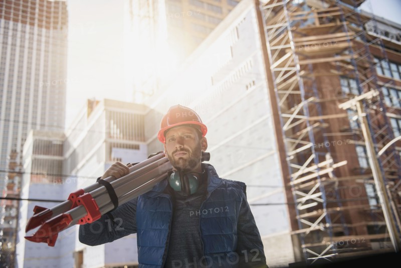 Construction worker carrying tripod on shoulder.