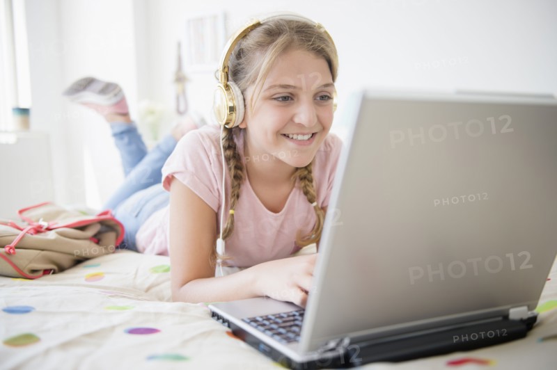 Girl (12-13) lying in bed using laptop