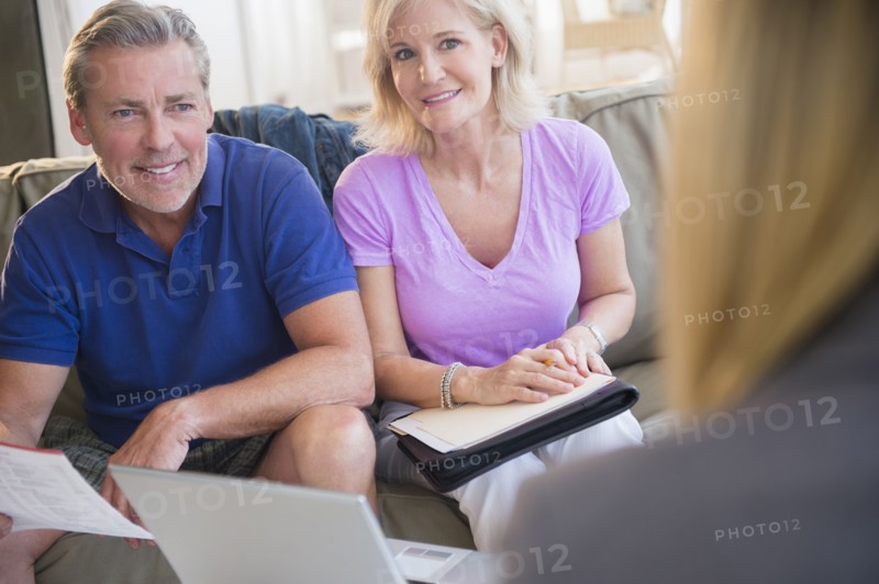 Portrait of couple sitting on sofa smiling at woman in blurred foreground