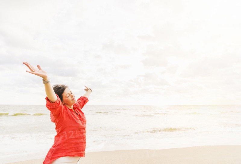 Side view of woman standing with arms up on beach