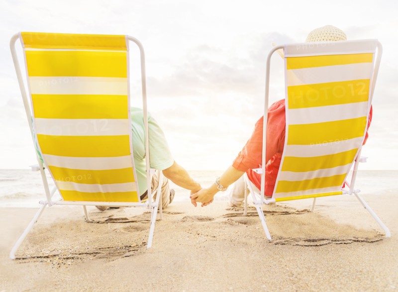 Rear view of couple sitting in lounge chairs on beach