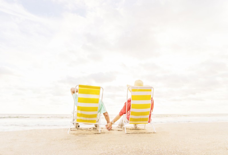 Rear view of couple sitting in lounge chairs on beach