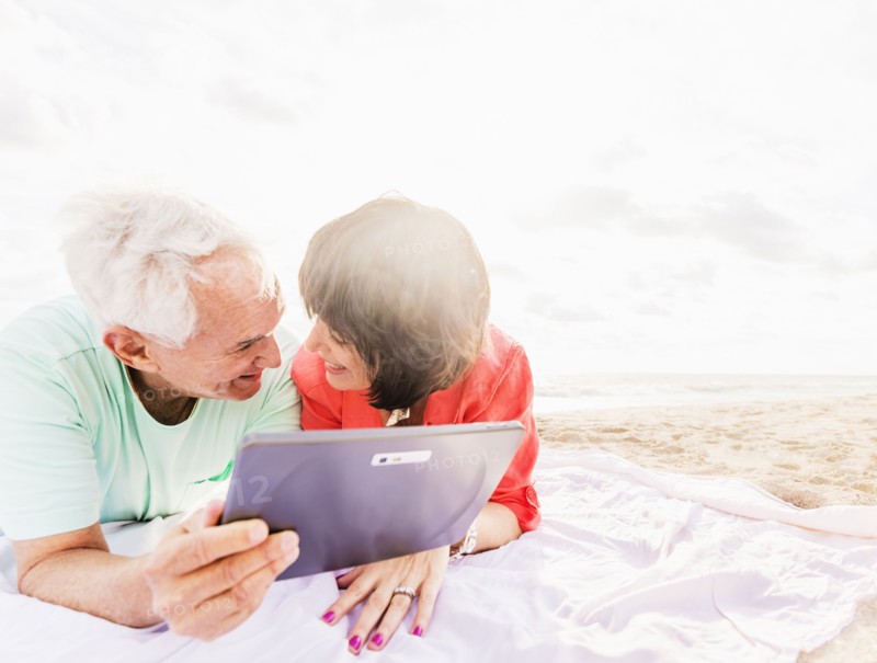 Couple with digital tablet lying on blanket at beach
