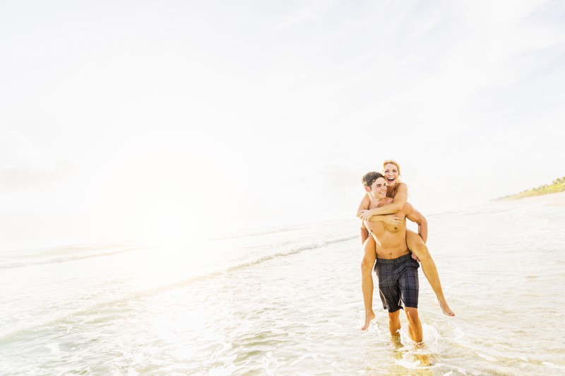 Boyfriend walking in surf carrying girlfriend piggyback