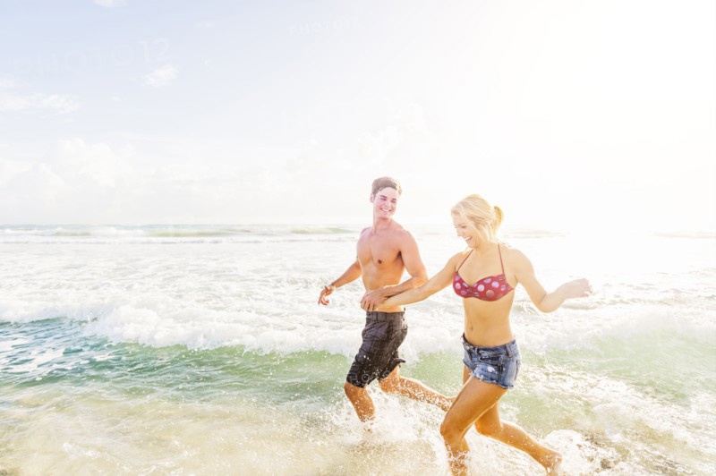 Young couple running in surf holding hands