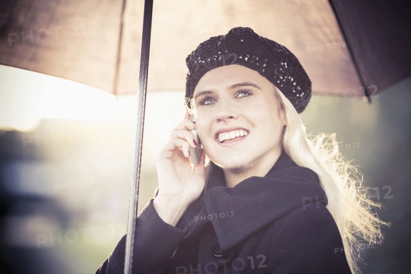 Smiling woman under umbrella using mobile phone