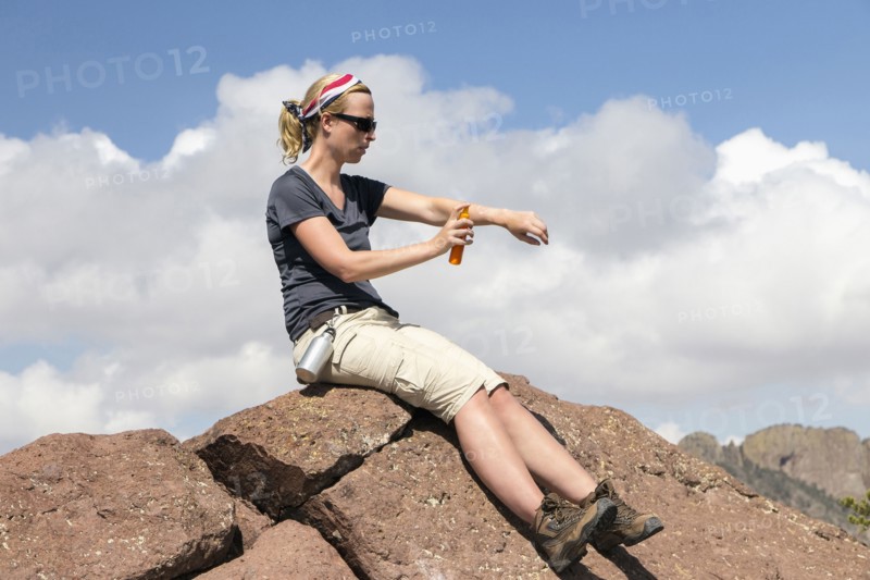 Woman sitting on rock and applying suntan lotion