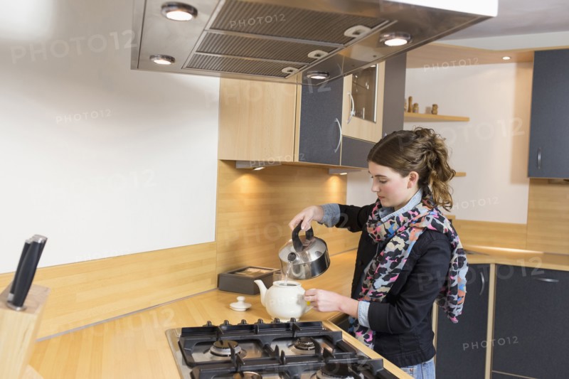 Woman pouring water at teapot in kitchen