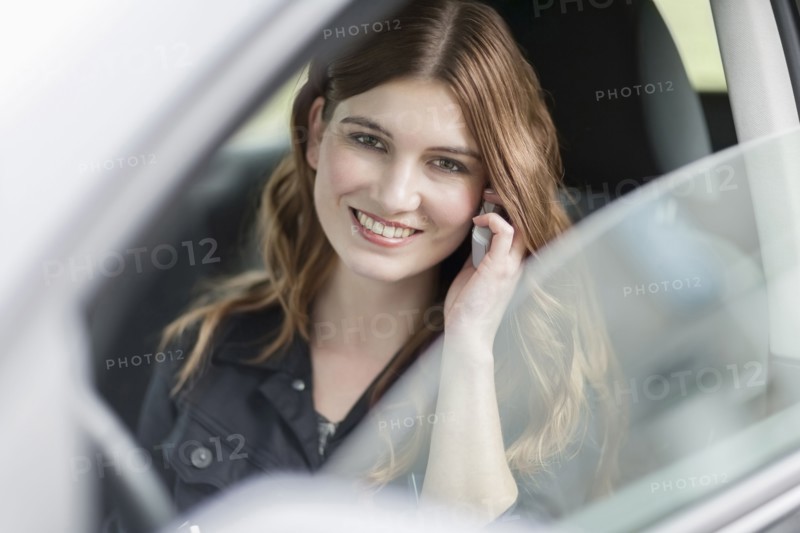 Young smiling woman speaking on phone in car