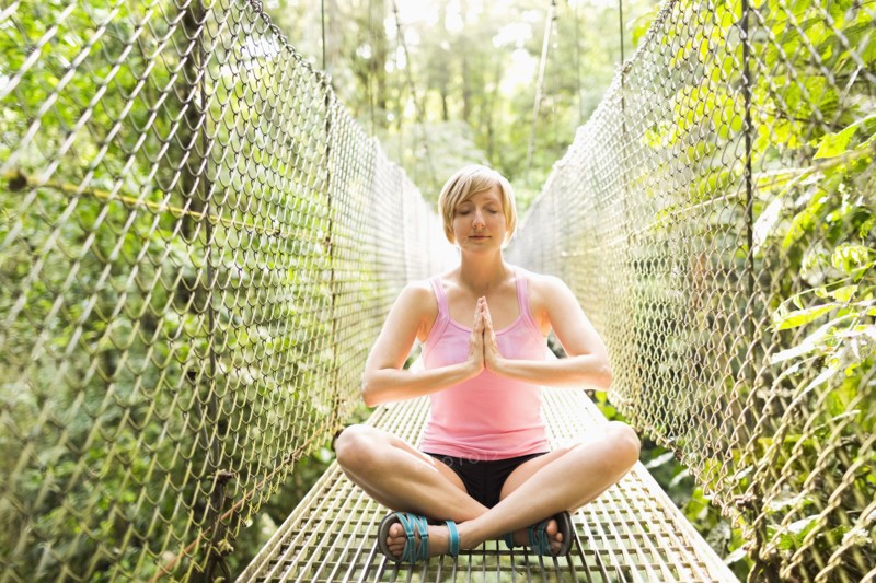 Woman practicing yoga on footbridge in forest