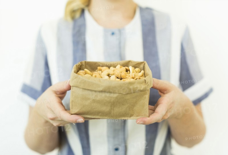 Studio shot of woman holding cashews in paper bag