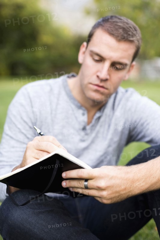 Portrait of young man writing journal in park
