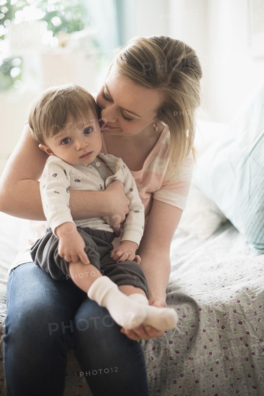 Mother sitting with little son (2-3 years) on bed.