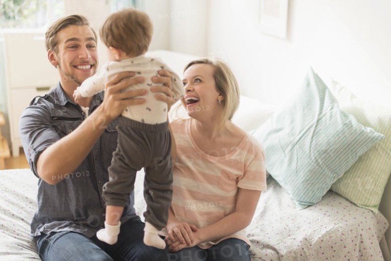 Happy parents playing with little son (2-3 years) on bed.