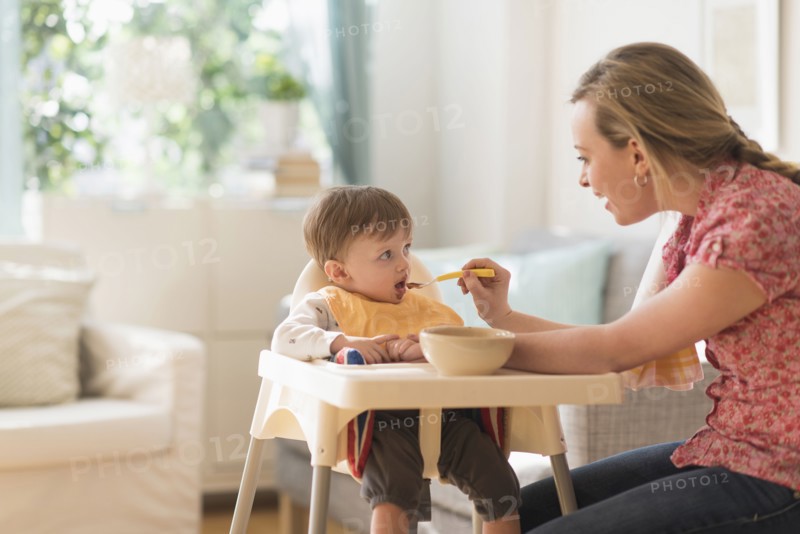 Mother feeding little boy (2-3 years) in high chair.