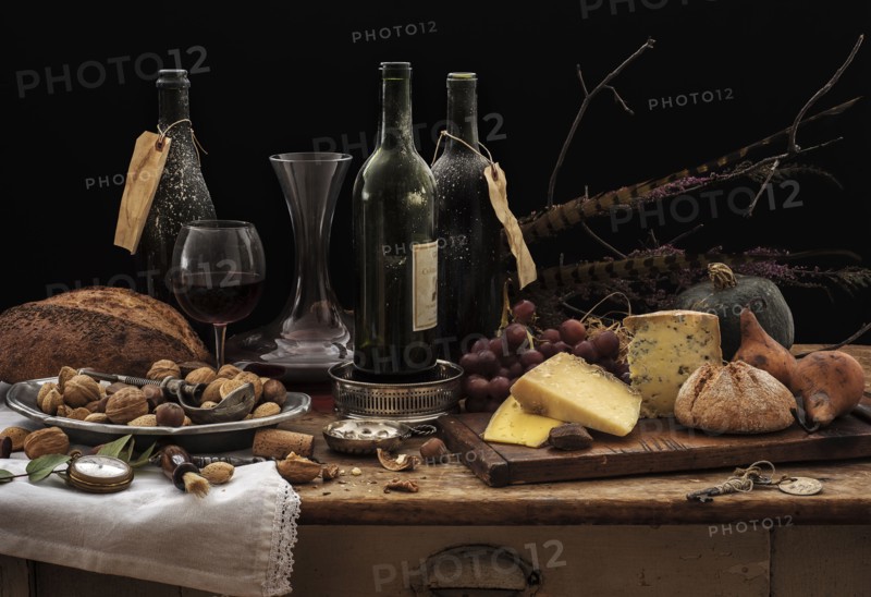 Still life with wine bottles, selection of cheese, bread and nuts on wooden table, studio shot.