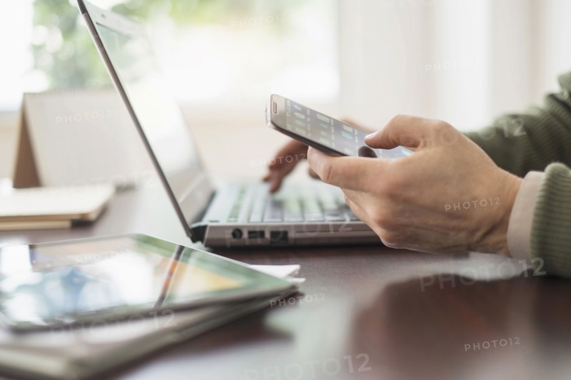 Close up of man's hands working at desk with electronic devices.