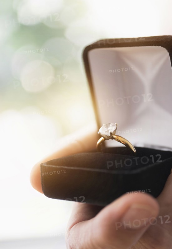 Close up of man's hand holding open box with engagement ring.