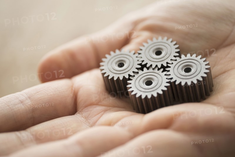 Close up of man's hand holding metal cogs.