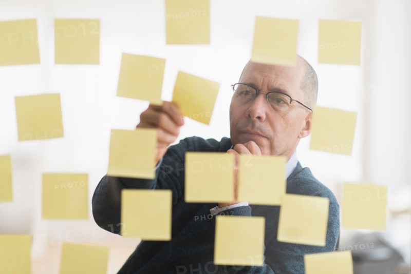 Businessman arranging adhesive notes on glass wall.